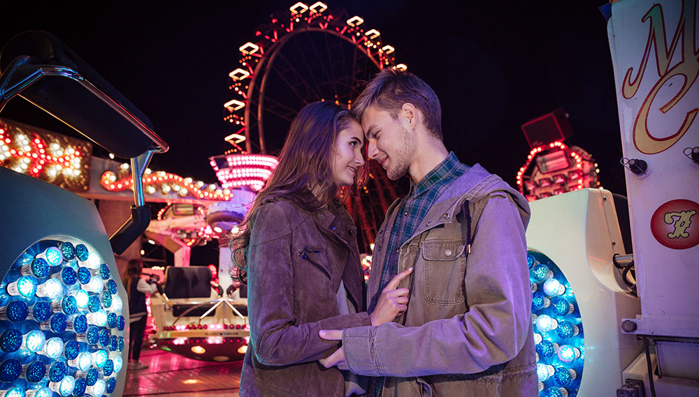 Smiling sensual young couple standing and embracing in amusement park